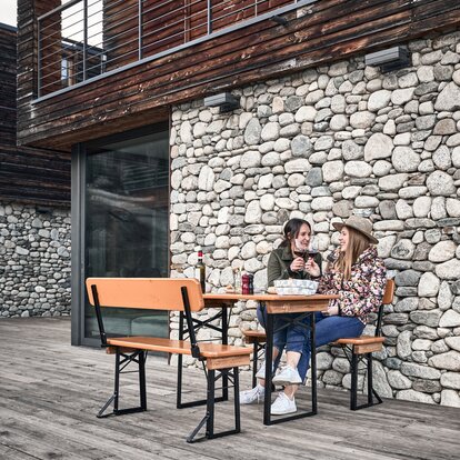 Two friends sit on the short beer tent set with backrest and clink glasses.