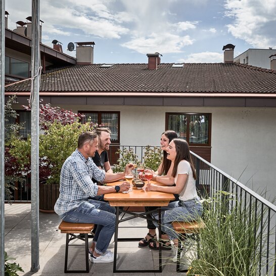 4 people sit on a short beer garden table set on the terrace and have a lot of fun.